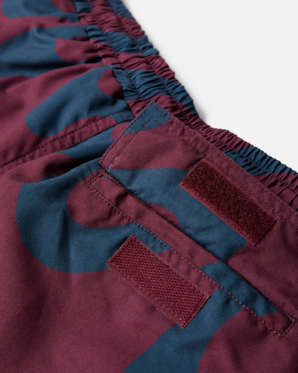 Detail of burgundy ByParra Splashed Swim Shorts showing the elastic waistband and velcro back pocket.